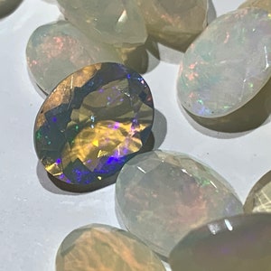 May include: A collection of oval-shaped opals, some with a rainbow iridescent sheen, others with a more muted, milky white appearance.