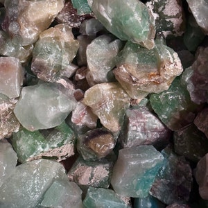 May include: A close-up of a pile of green, translucent, and opaque crystals. The crystals are various sizes and shapes, with some having a rough texture.