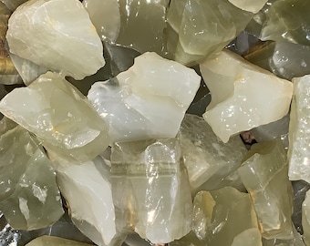 May include: A close-up of a pile of green and white translucent tumbled stones. The stones are smooth and have a natural, organic shape.