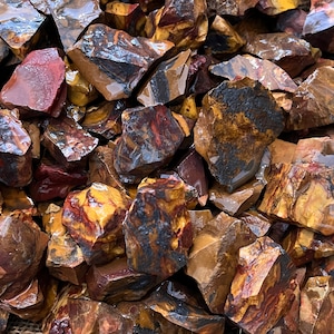 May include: A close-up of a pile of rough, natural, red, yellow, and black striped jasper stones.