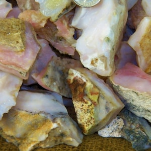 May include: A pile of pink, white, and brown opal rough. The opal is translucent and has a variety of textures.