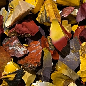 May include: A close-up of a pile of colorful, polished stones. The stones are a mix of red, yellow, and purple, and they have a variety of shapes and sizes.