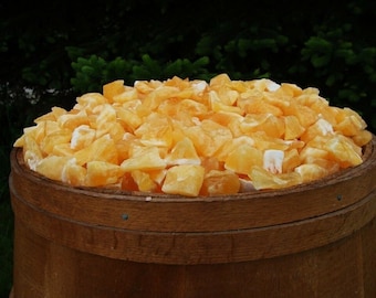 May include: A wooden barrel filled with a large quantity of rough, orange calcite crystals. The crystals have a translucent quality and varying shapes. The barrel is made of light brown wood and is set against a dark green background.