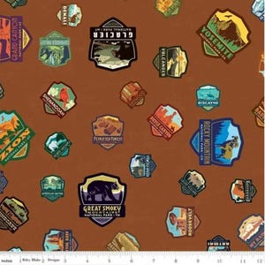 May include: Brown fabric featuring a repeating pattern of colorful national park patches. Patches include "Grand Canyon", "Yosemite", "Great Smoky Mountains", and "Rocky Mountain". The patches are in various shapes and sizes.