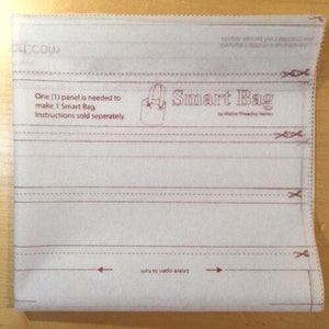 May include: A white fabric panel with brown lines and text. The text reads "One (1) panel is needed to make 1 Smart Bag. Instructions sold separately." and "Smart Bag by Mattie Rhoades Haines".