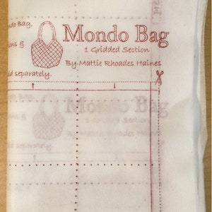 May include: A white fabric pattern sheet with a red grid and the text "Mondo Bag 1 Gridded Section By Mattie Rhoades Haines".
