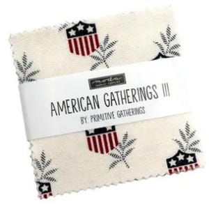 May include: A stack of fabric squares with a cream background, featuring a repeating pattern of red, white, and blue shield emblems and black leaf designs. The label reads "AMERICAN GATHERINGS III" by Primitive Gatherings.
