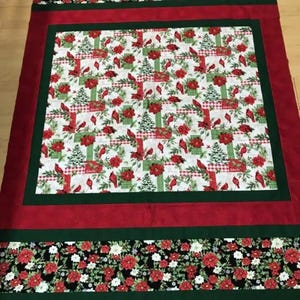 May include: A red, green, and white Christmas quilt with a pattern of cardinals, poinsettias, and pine trees. The quilt has a black and white floral border.