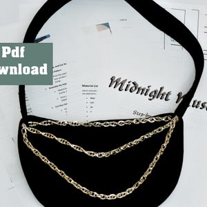 May include: A black fabric bag with a gold chain strap. The bag is on a white surface with a printed sheet of paper that says "Midnight Muse" and "Step-by-Step".