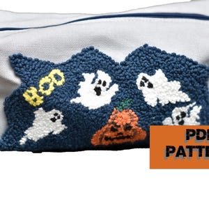 Puede incluir: Una bolsa de lona blanca con cremallera con un diseño bordado en azul y blanco de fantasmas y una calabaza. El diseño dice "Boo!" en hilo amarillo. La bolsa es un patrón PDF.