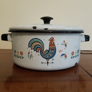 May include: White enamel pot with a black lid and a rooster design. The rooster is colorful with blue, red, yellow, and green accents. The pot has a black rim and handle.