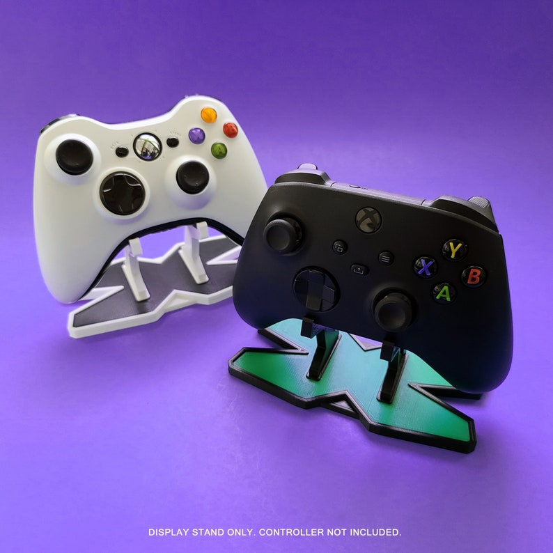 May include: A white and a black video game controller stand with a green X logo. DISPLAY STAND ONLY. CONTROLLER NOT INCLUDED.