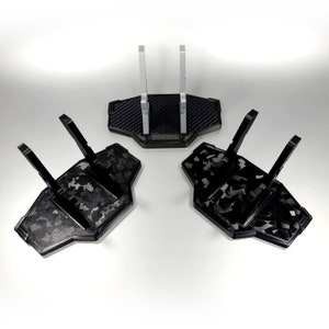 May include: Three black plastic display stands with a camouflage pattern. The stands have two vertical supports and a base. The stands are designed to hold action figures or other collectibles.