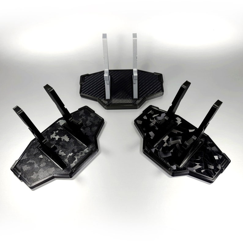 May include: Three black plastic display stands with a camouflage pattern. The stands have two vertical supports and a base. The stands are designed to hold action figures or other collectibles.