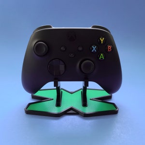 May include: A black Xbox controller with green and black X logo stand. The controller has buttons labeled A, B, X, and Y.
