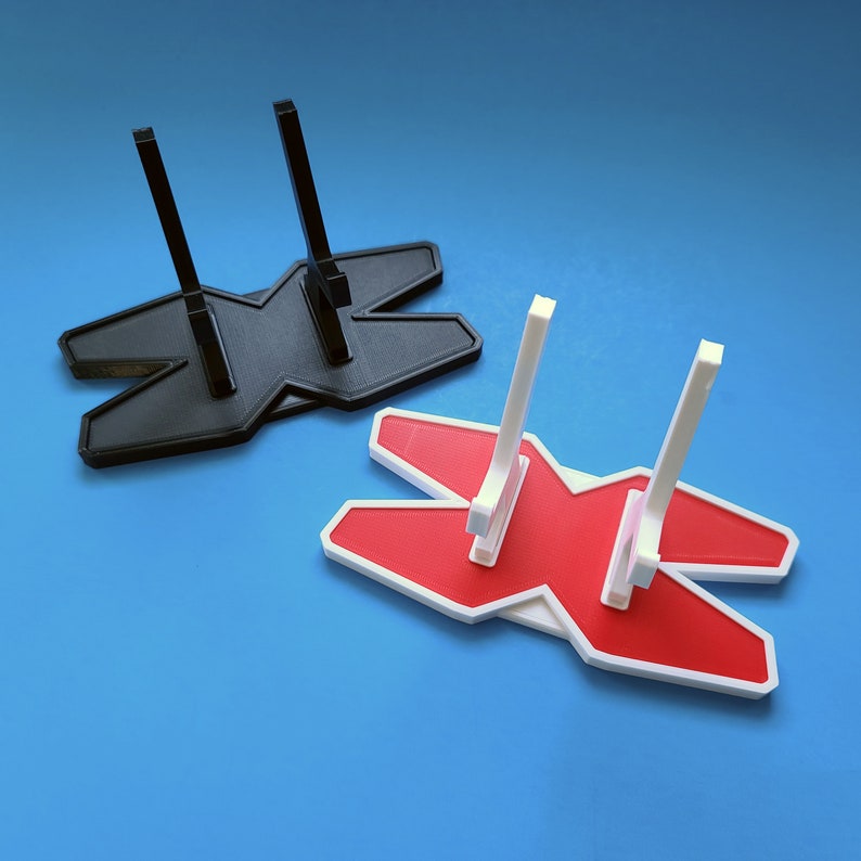 May include: Two 3D printed display stands shaped like the letter X. One stand is black and the other is red with a white border.