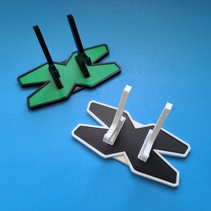 May include: Two 3D printed display stands, one green and one white, shaped like the letter 'X' with two vertical supports.