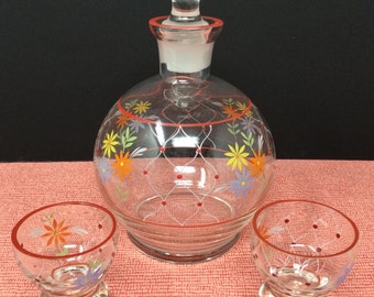 May include: A set of three clear glass decanters with a floral design. The decanters have a red rim and a red and white lattice pattern. The largest decanter has a stopper with a red rim.
