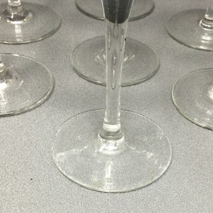 May include: A set of six clear glass wine glasses with a long stem and a round bowl. The glasses are arranged in a circle on a gray surface.
