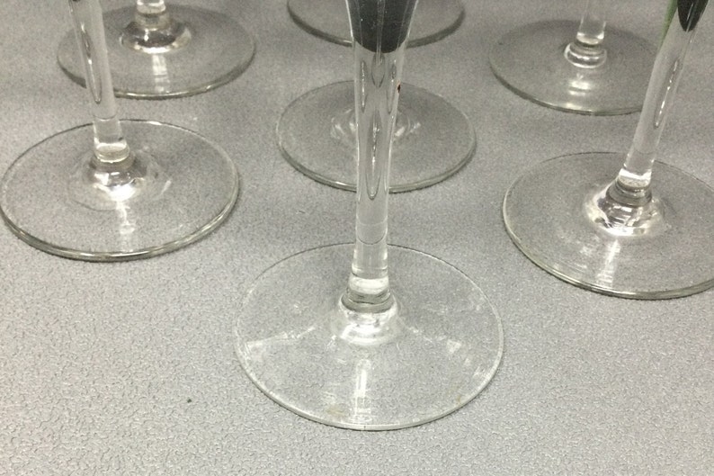 May include: A set of six clear glass wine glasses with a long stem and a round bowl. The glasses are arranged in a circle on a gray surface.