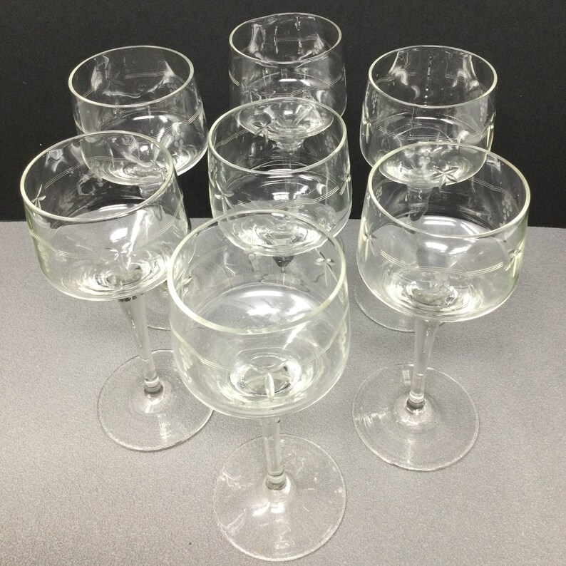May include: Set of six clear glass wine glasses with etched designs. The glasses have a tall, slender stem and a wide bowl.