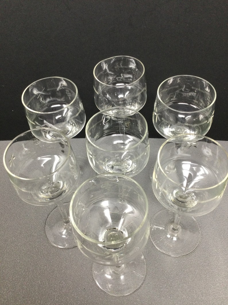 May include: Set of six clear glass wine glasses with etched designs. The glasses have a round bowl and a long stem.