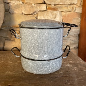 Op de afbeelding: Een vintage grijze emaille dubbele ketel met zwarte handvatten. De ketel heeft een gespikkeld wit patroon.