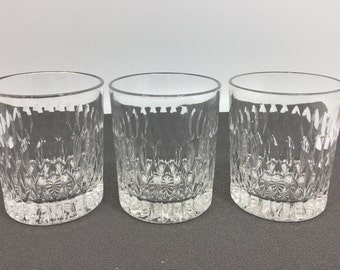 May include: Three clear, patterned drinking glasses. Each glass has a thick, textured base and a repeating vertical design on the sides. The glasses are arranged in a row, showcasing their intricate details.