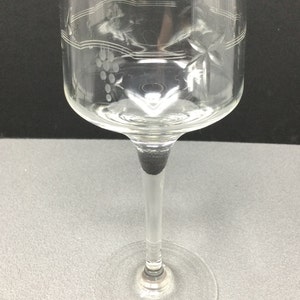 May include: A clear glass wine glass with a long stem and a wide bowl. The bowl has an etched design of grapes and vines.