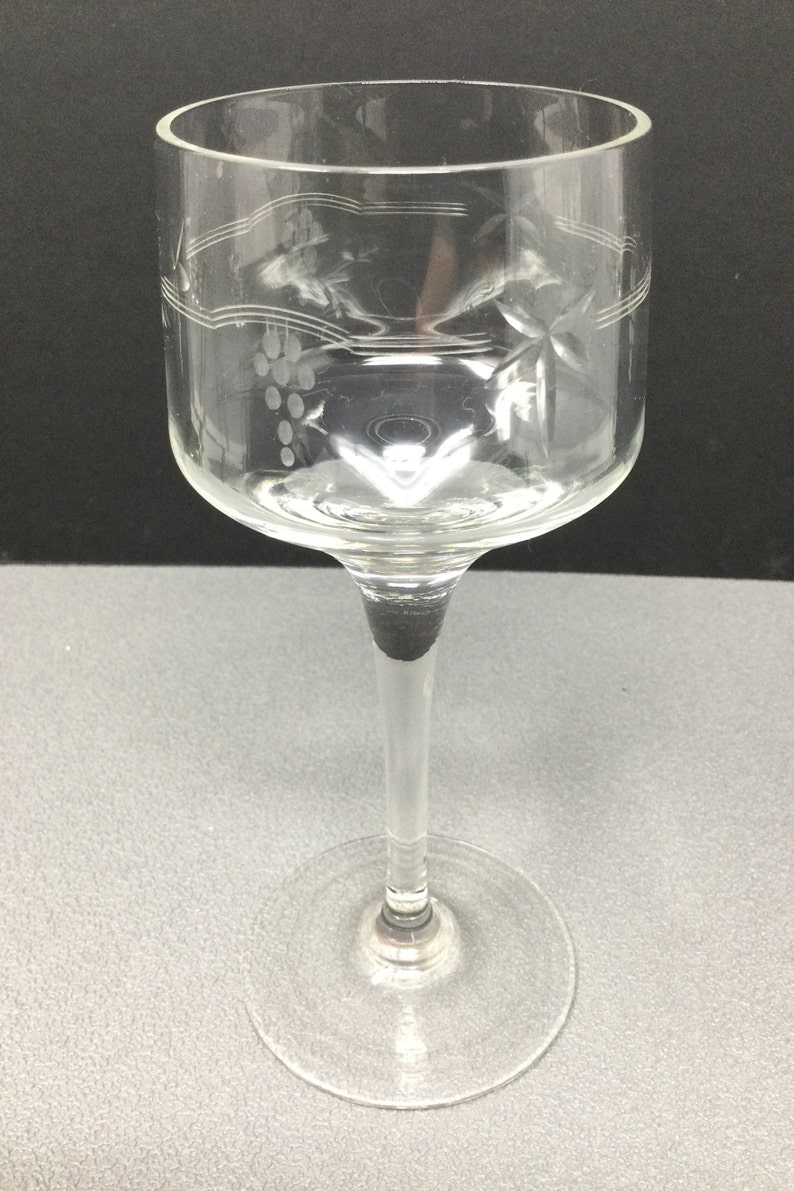 May include: A clear glass wine glass with a long stem and a wide bowl. The bowl has an etched design of grapes and vines.
