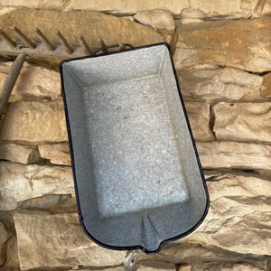 Op de afbeelding: Een vintage emaille bakvorm met een zwarte rand en een gespikkeld grijs interieur. De vorm is leeg en staat op een stenen oppervlak.