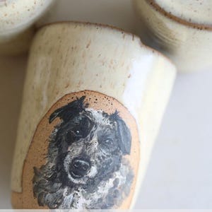 May include: Set of four ceramic mugs with a hand-painted dog portrait on each. The mugs are a light beige color with a brown rim. The text "PET LOVER GIFT IDEAS" is displayed below the mugs.