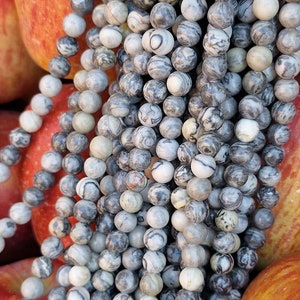 May include: A strand of gray and white striped gemstone beads. The beads are round and have a natural, polished finish.