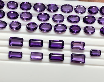 Könnte beinhalten: Eine Sammlung von Amethyst-Edelsteinen in ovalen und rechteckigen Formen. Die Edelsteine sind auf einer weißen Oberfläche angeordnet.