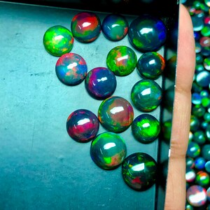 May include: A collection of 15 round, iridescent black opals with green, red, and blue flashes. The opals are displayed in a black tray.