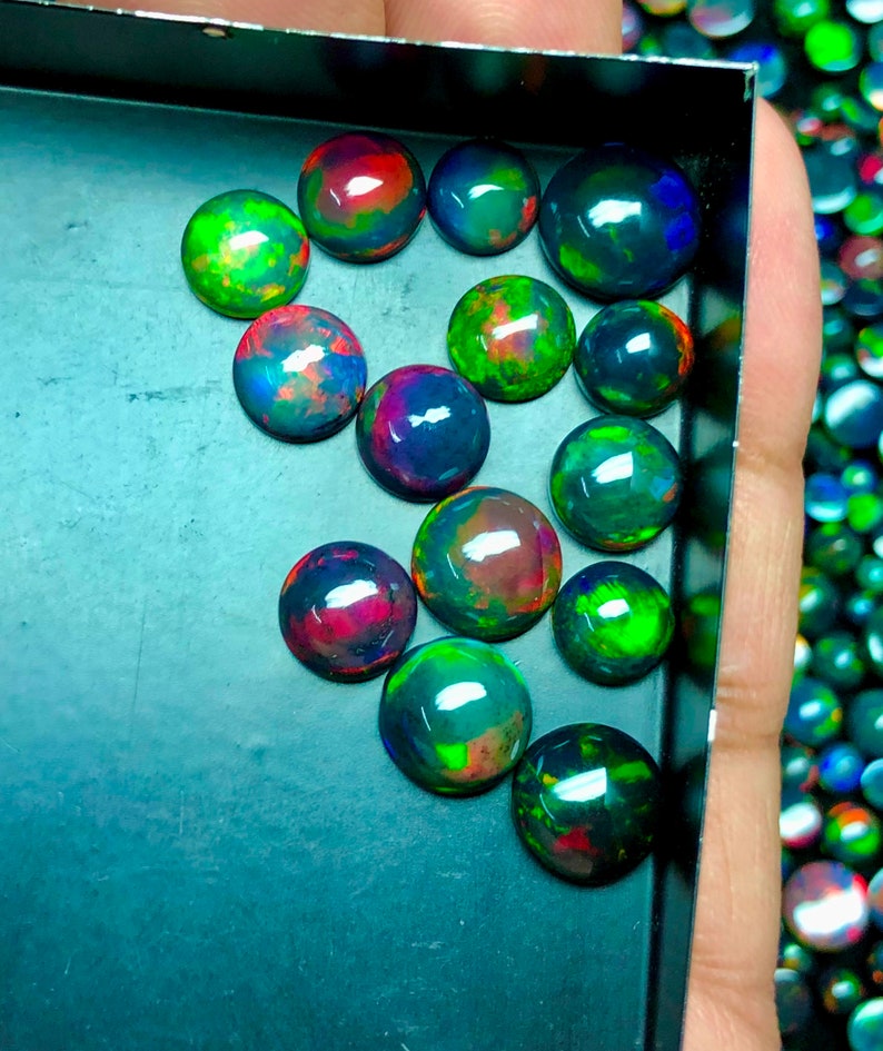 May include: A collection of 15 round, iridescent black opals with green, red, and blue flashes. The opals are displayed in a black tray.