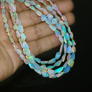 May include: Strands of opal beads with a pearlescent sheen. The beads have a mix of white, blue, and iridescent colors. The opal beads are strung together, creating a necklace or jewelry component.