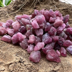 Può includere: Un mucchio di pietre preziose grezze rosa e viola. Le pietre sono di varie dimensioni e forme e hanno un aspetto naturale e non levigato.