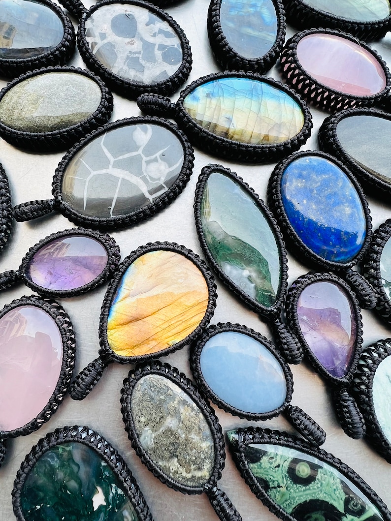 Peut inclure: Assortiment de pendentifs en pierres pr&eacute;cieuses color&eacute;es avec cordon noir, pr&eacute;sentant diverses formes et motifs, notamment une goutte, un ovale et un rond.