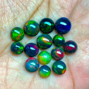 May include: A collection of 14 round black opal cabochons, each displaying a variety of iridescent colors, including green, blue, red, and orange.