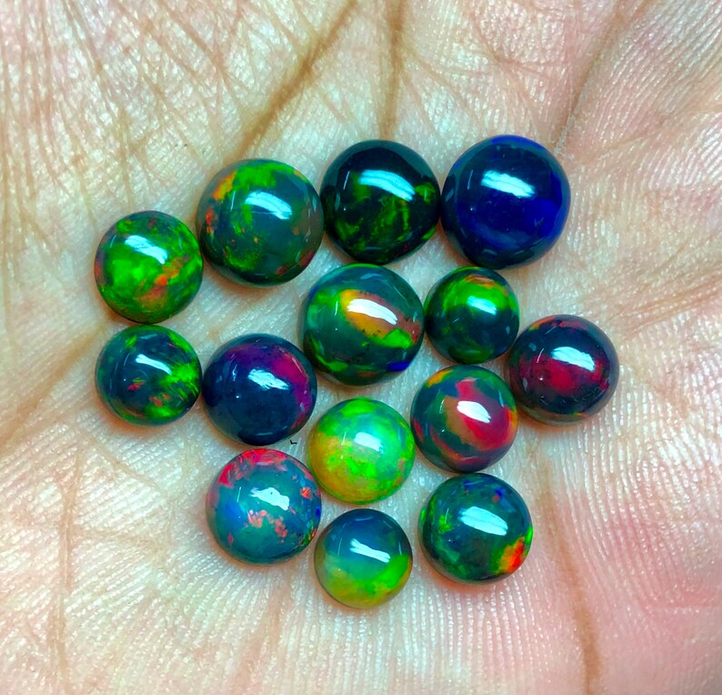 May include: A collection of 14 round black opal cabochons, each displaying a variety of iridescent colors, including green, blue, red, and orange.