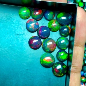 May include: A collection of 15 round, iridescent black opals with green, red, and blue flashes of color. The opals are arranged in a tray.