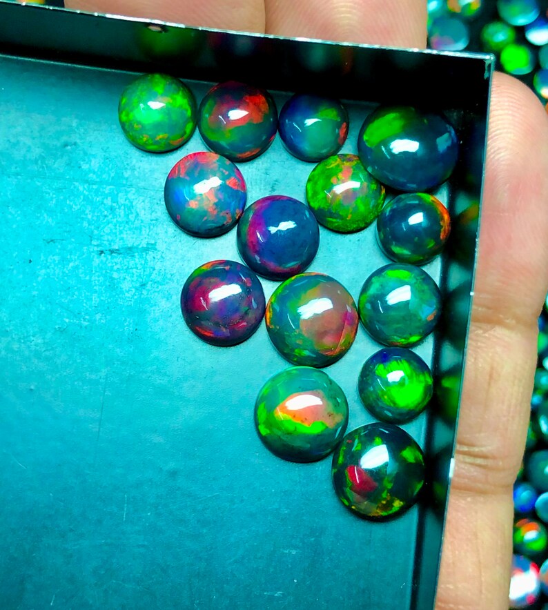 May include: A collection of 15 round, iridescent black opals with green, red, and blue flashes of color. The opals are arranged in a tray.