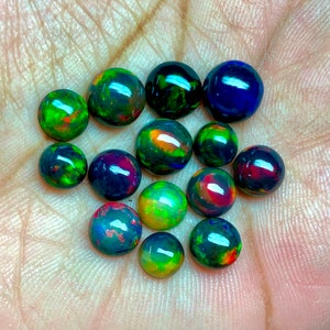 May include: A collection of 13 round, black opal gemstones with iridescent green, blue, red, and orange colors.