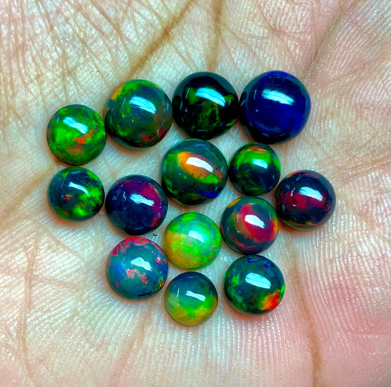 May include: A collection of 13 round, black opal gemstones with iridescent green, blue, red, and orange colors.