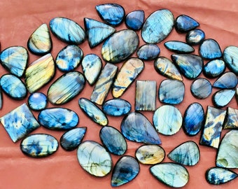 Peut inclure: Une collection de cabochons de labradorite en différentes formes et tailles. Les pierres sont un mélange de couleurs bleues, vertes et dorées avec des reflets irisés.