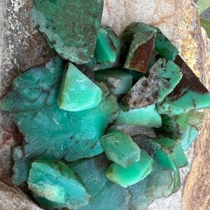 May include: A collection of green, polished, natural chrysoprase stones. The stones are various sizes and shapes, with some having a more opaque appearance than others.
