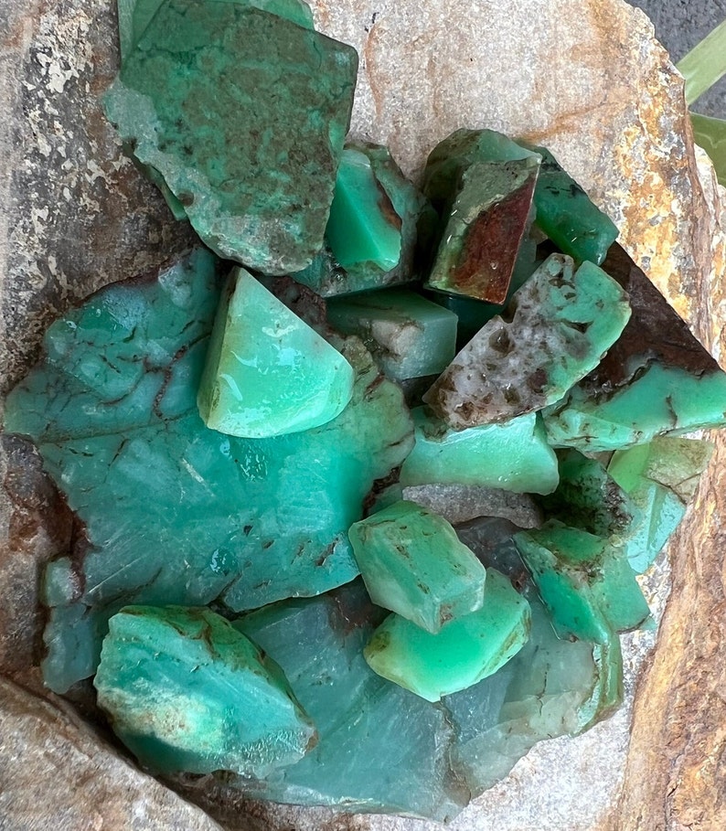 May include: A collection of green, polished, natural chrysoprase stones. The stones are various sizes and shapes, with some having a more opaque appearance than others.