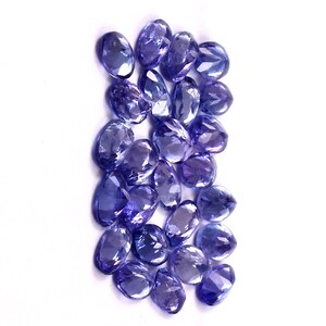 Puede incluir: Una colecci&oacute;n de piedras preciosas sueltas, facetadas, de forma ovalada, de color p&uacute;rpura. Las piedras preciosas est&aacute;n dispuestas en un mont&oacute;n suelto.
