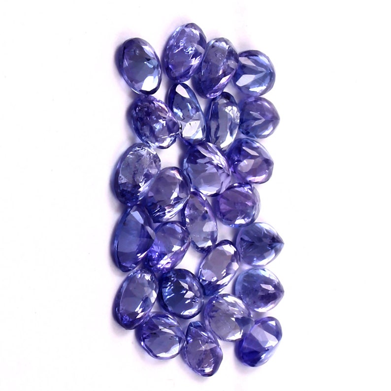 Puede incluir: Una colecci&oacute;n de piedras preciosas sueltas, facetadas, de forma ovalada, de color p&uacute;rpura. Las piedras preciosas est&aacute;n dispuestas en un mont&oacute;n suelto.